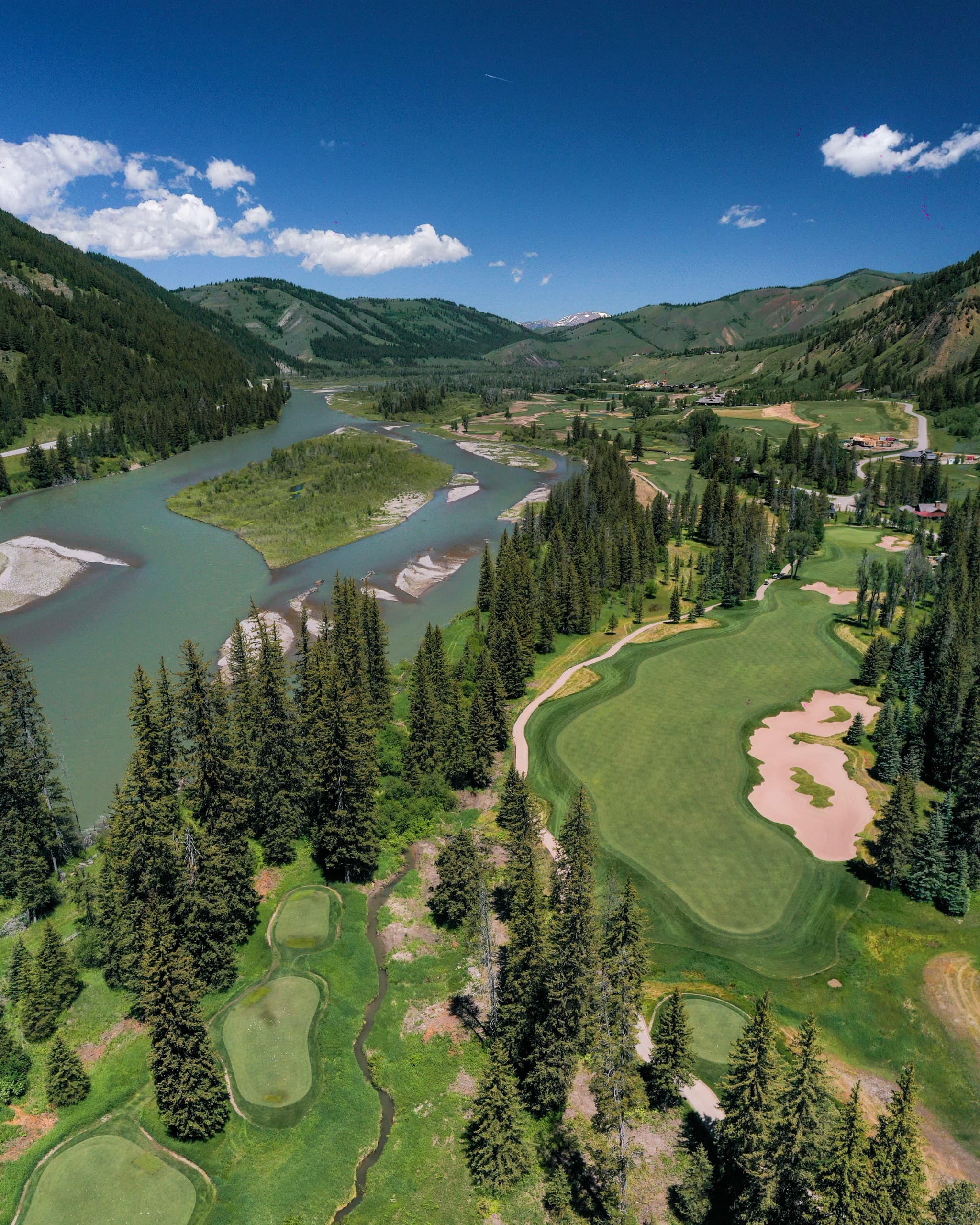 An aerial view of the Snake River Sporting Club's golfing greens, surrounded by mountains, intersected by river streams and sand hazards