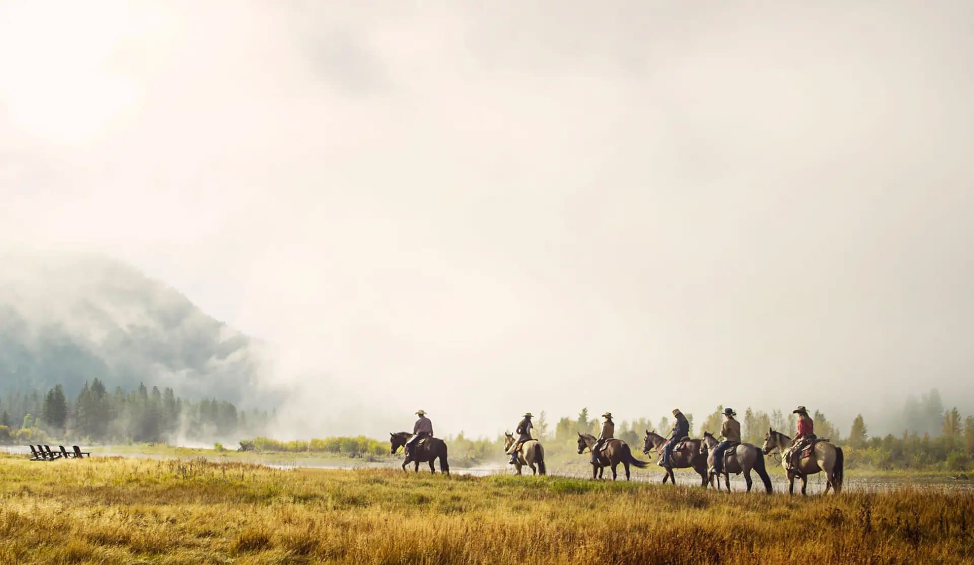 A group of guests ride horseback across a field into the fog