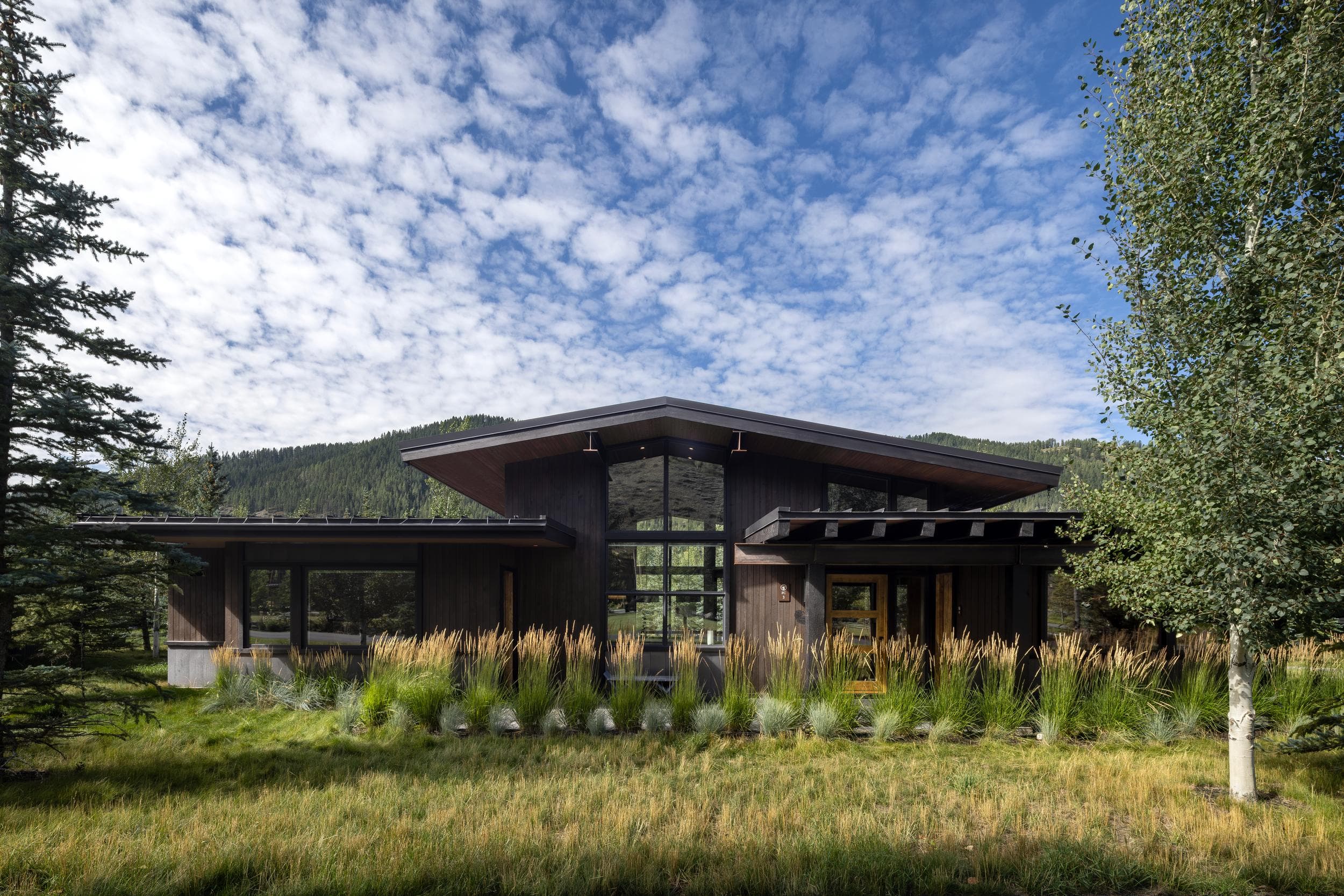 Modern mountain cabin among ornamental grasses under a blue sky at Snake River Sporting Club in Jackson Hole, Wyoming