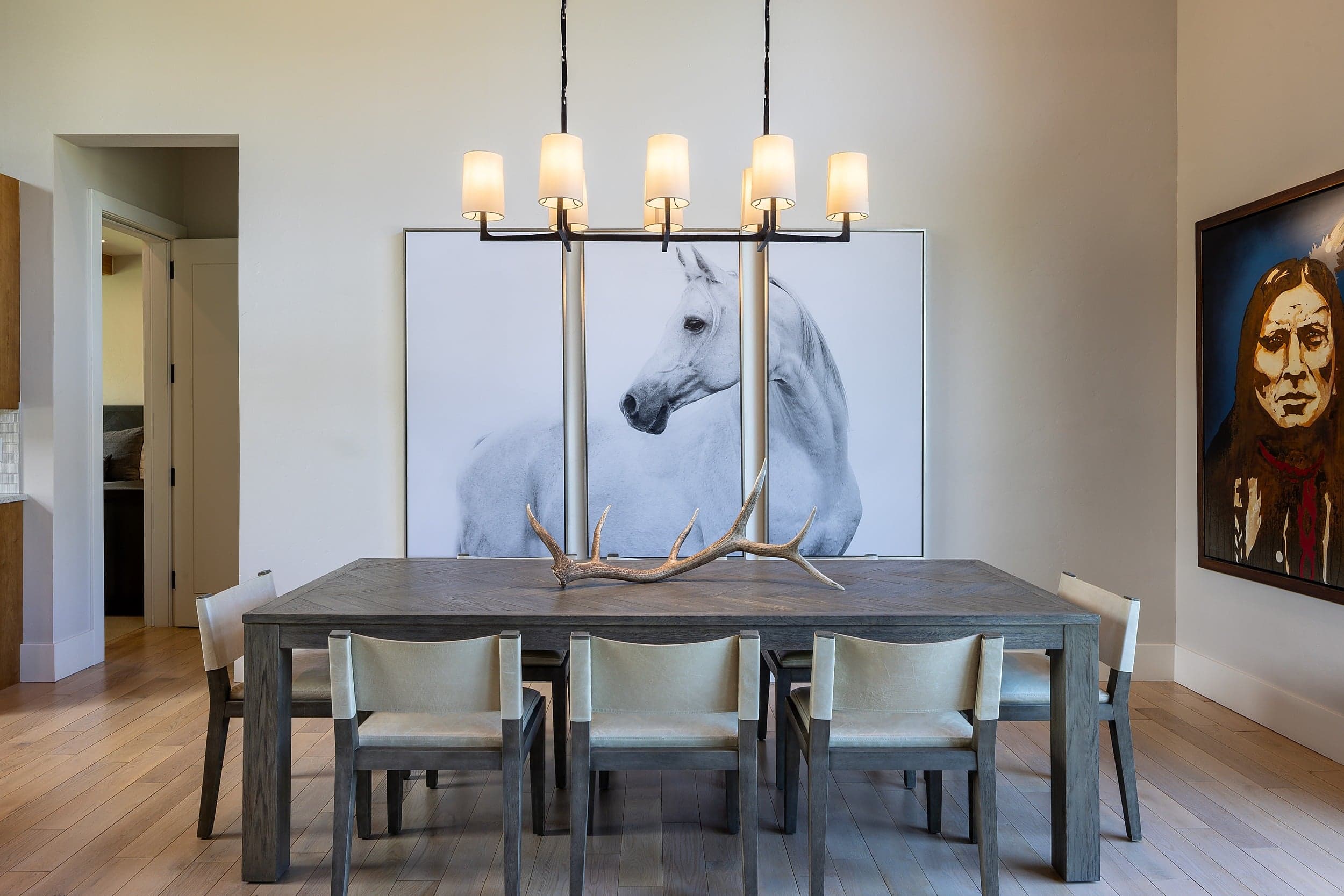 Private dining room with a candle-style chandelier, an antler centerpiece and a white horse triptych at Snake River Sporting Club in Jackson Hole, Wyoming