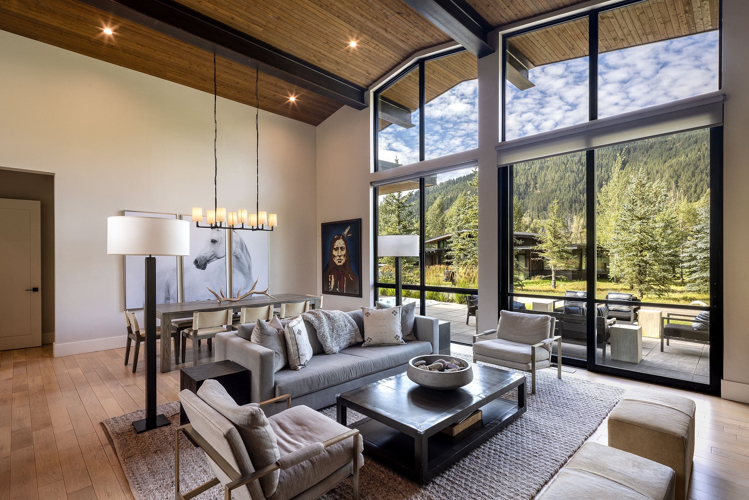 Vaulted great room with floor-to-ceiling windows framing forested mountains at Snake River Sporting Club in Jackson Hole, Wyoming